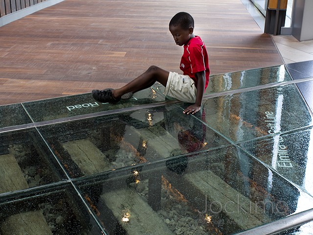 Boy Sitting on Clear Glass Flooring by Jockimo at the Waterloo Museum